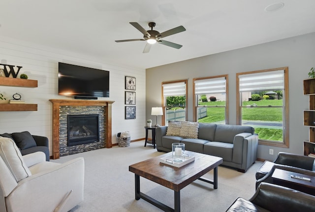 living room with ceiling fan, light carpet, a tile fireplace, wood walls, and baseboards