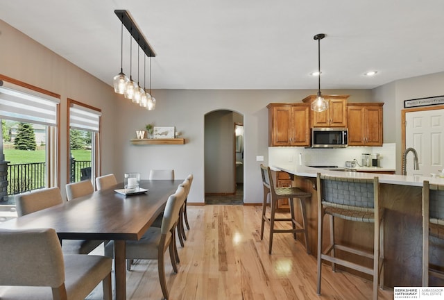 dining area with arched walkways, light wood-type flooring, baseboards, and recessed lighting