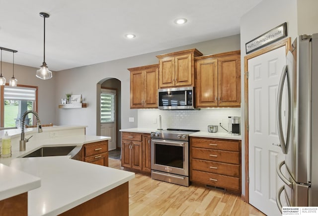 kitchen with stainless steel appliances, a sink, brown cabinets, arched walkways, and tasteful backsplash