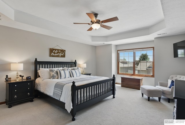 bedroom with a tray ceiling, light carpet, baseboards, and a ceiling fan