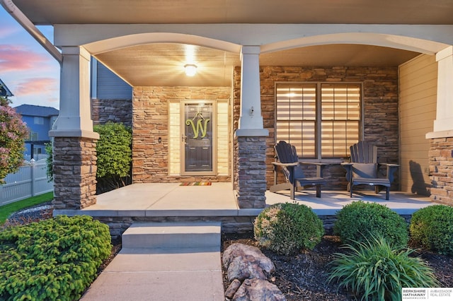 exterior entry at dusk with covered porch and stone siding