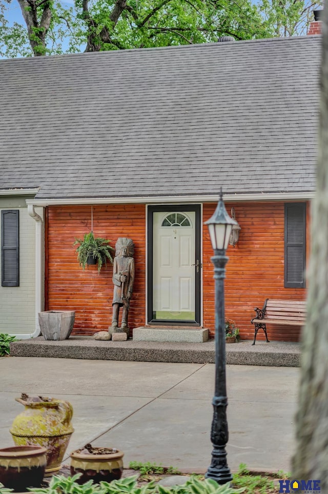 view of exterior entry featuring a patio area and a shingled roof