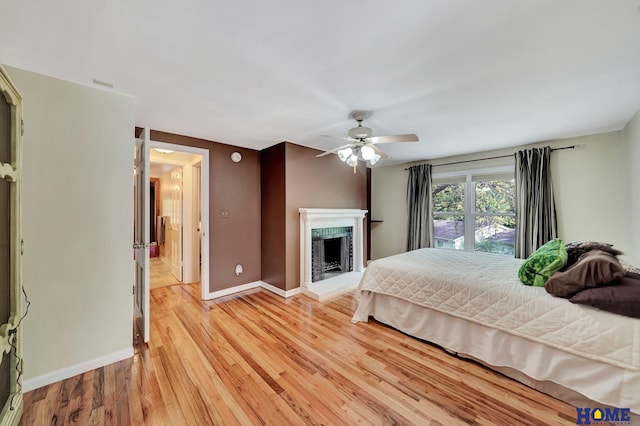 bedroom featuring baseboards, light wood-style flooring, a fireplace, and ceiling fan