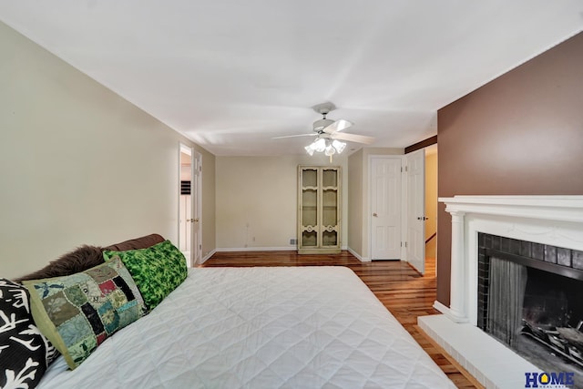 bedroom featuring wood finished floors, a ceiling fan, a fireplace with raised hearth, and baseboards