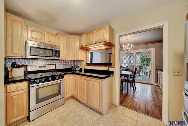 kitchen featuring appliances with stainless steel finishes, light brown cabinetry, a chandelier, dark countertops, and decorative backsplash