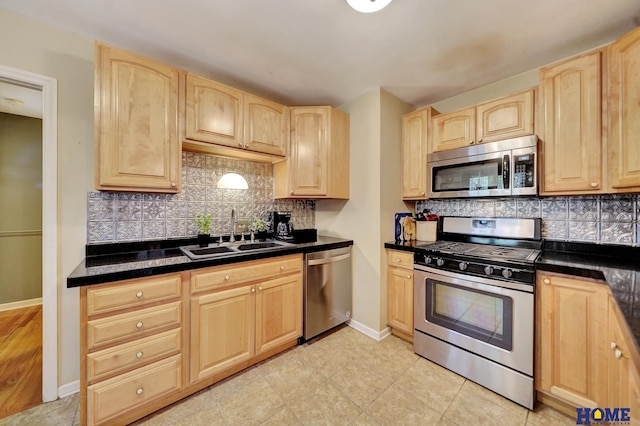kitchen with appliances with stainless steel finishes, light brown cabinets, a sink, dark countertops, and tasteful backsplash