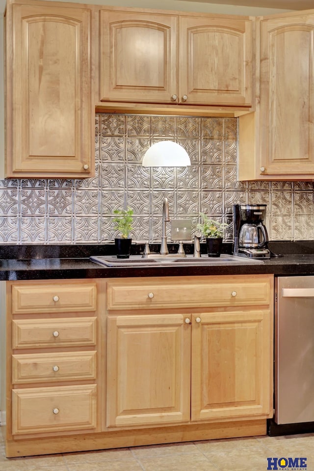 kitchen featuring stainless steel dishwasher, light brown cabinets, a sink, and dark countertops