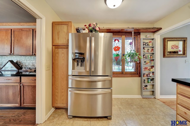 kitchen featuring stainless steel refrigerator with ice dispenser, dark countertops, backsplash, baseboards, and light tile patterned floors