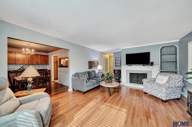 living area featuring a chandelier, a brick fireplace, light wood-style flooring, ornamental molding, and built in features