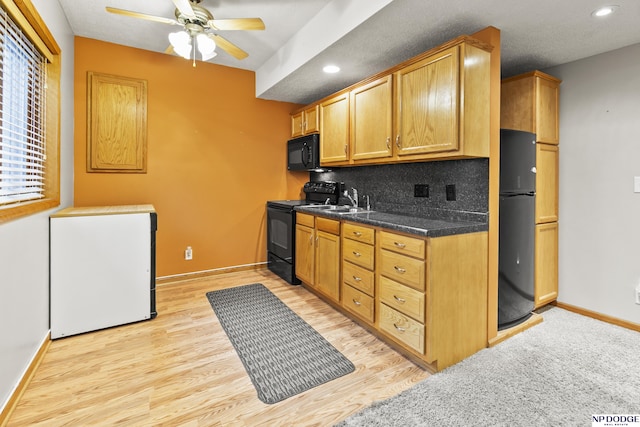 kitchen featuring black appliances, light wood-style floors, baseboards, ceiling fan, and dark countertops