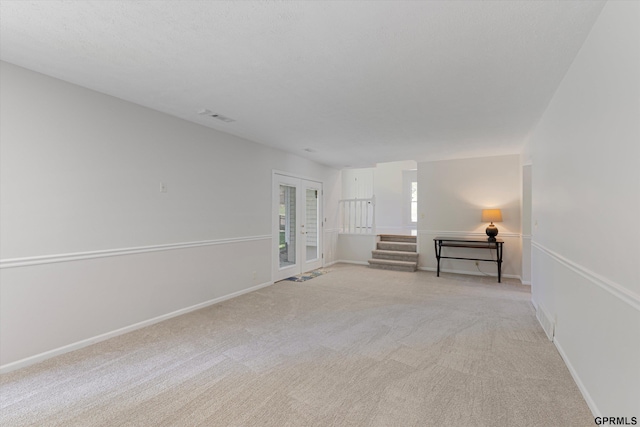 spare room featuring french doors, light carpet, stairs, and baseboards