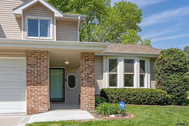 doorway to property featuring a garage, a yard, and brick siding