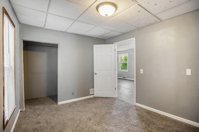 unfurnished bedroom with a drop ceiling, carpet flooring, baseboards, and a closet