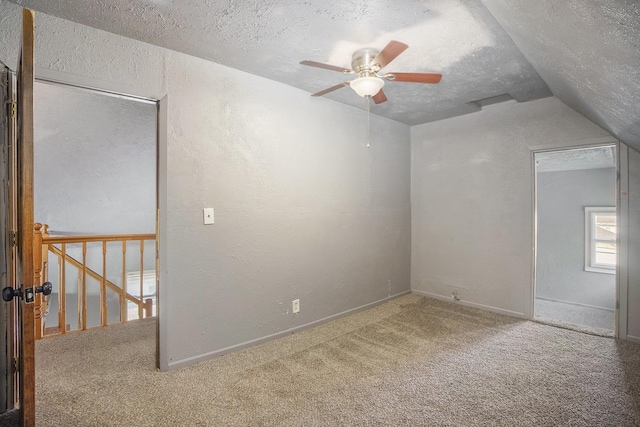 carpeted spare room featuring ceiling fan, a textured ceiling, a textured wall, lofted ceiling, and baseboards