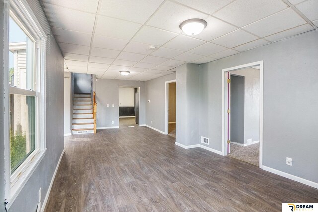 unfurnished living room with a drop ceiling, wood finished floors, stairs, and baseboards