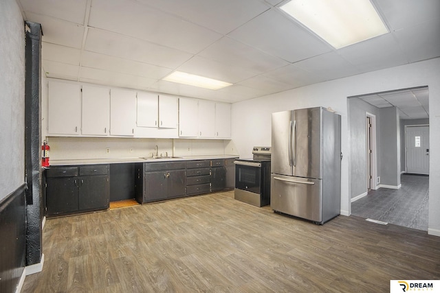 kitchen with appliances with stainless steel finishes, a drop ceiling, white cabinetry, a sink, and light wood-type flooring
