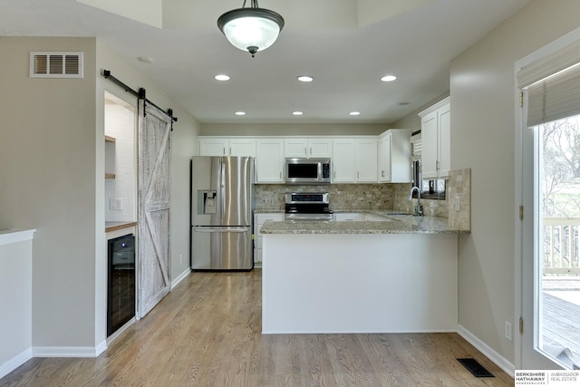 8114 S 167th St, Omaha, NE 68136 - kitchen with stainless steel appliances, a barn door, light stone counters, decorative backsplash, and white cabinetry