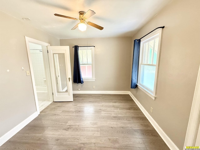 unfurnished bedroom featuring multiple windows, wood finished floors, baseboards, and a ceiling fan
