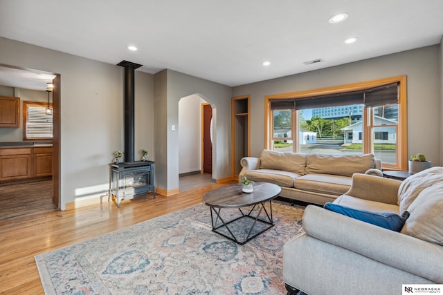 living area with a wood stove, arched walkways, recessed lighting, light wood finished floors, and baseboards