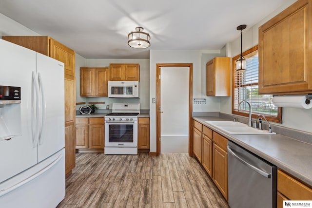 kitchen featuring white appliances, a sink, wood finished floors, decorative light fixtures, and brown cabinets