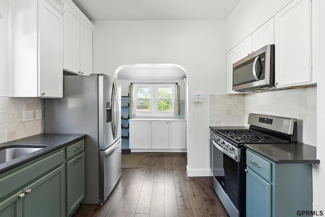 kitchen featuring stainless steel appliances, dark countertops, arched walkways, and white cabinetry