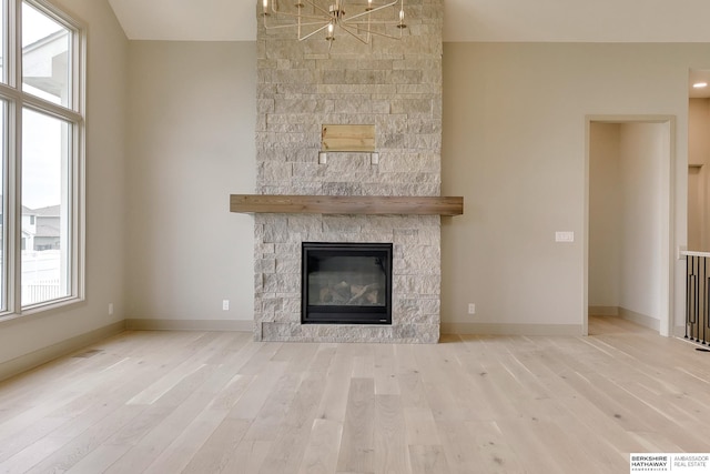 unfurnished living room with wood finished floors, a stone fireplace, a chandelier, and baseboards