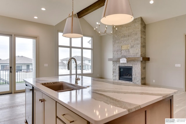 kitchen with a sink, beam ceiling, open floor plan, light stone countertops, and a stone fireplace