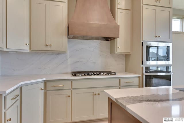 kitchen with stainless steel appliances, custom exhaust hood, decorative backsplash, and light stone counters