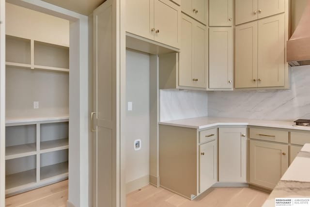 kitchen featuring wall chimney range hood, decorative backsplash, light countertops, and cooktop
