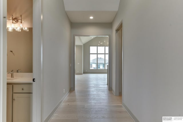 corridor with light wood-style flooring, recessed lighting, baseboards, and a sink