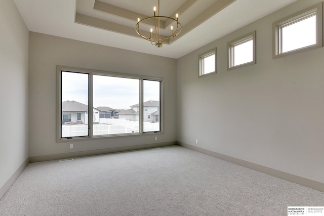 spare room featuring a chandelier, a raised ceiling, carpet floors, and baseboards