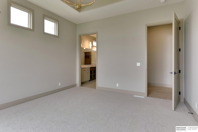 unfurnished bedroom with light colored carpet, ensuite bath, and baseboards