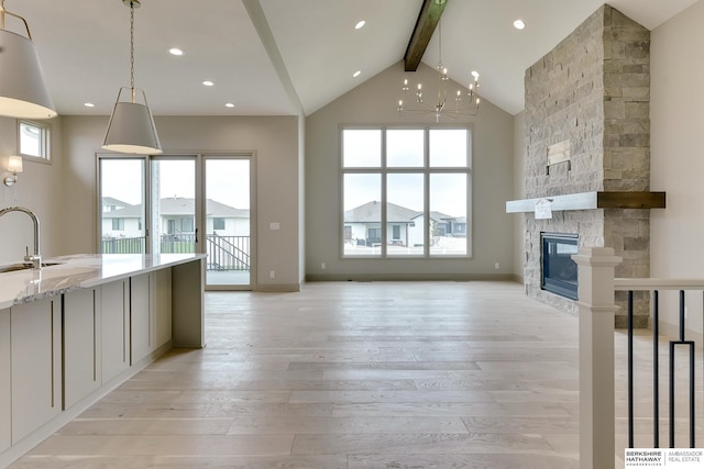 unfurnished living room featuring beamed ceiling, light wood-type flooring, a chandelier, a fireplace, and high vaulted ceiling