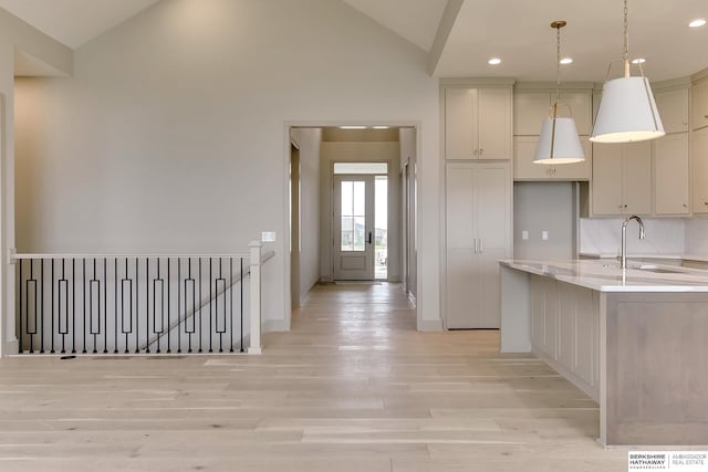 kitchen featuring a sink, light wood finished floors, lofted ceiling, baseboards, and recessed lighting