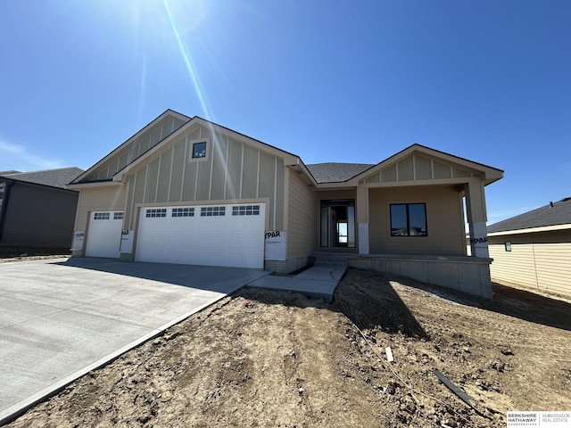 view of front of home with board and batten siding, an attached garage, concrete driveway, covered porch, and roof with shingles