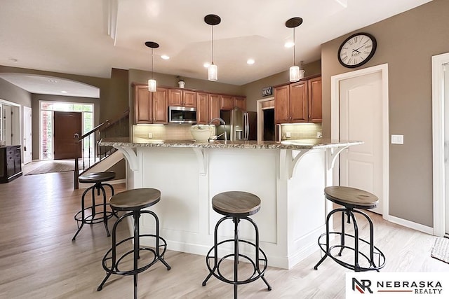 kitchen with appliances with stainless steel finishes, brown cabinetry, a breakfast bar area, backsplash, and recessed lighting