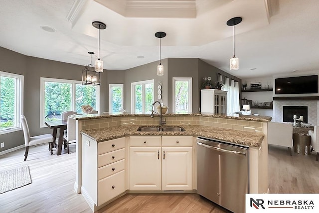 kitchen featuring stainless steel dishwasher, a sink, light wood-type flooring, light stone counters, and pendant lighting