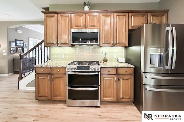 kitchen with appliances with stainless steel finishes, light wood finished floors, arched walkways, and decorative backsplash