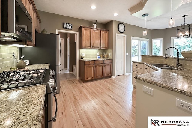 kitchen with a sink, gas stove, backsplash, brown cabinets, and light stone counters