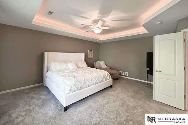 carpeted bedroom featuring a tray ceiling, baseboards, and a ceiling fan