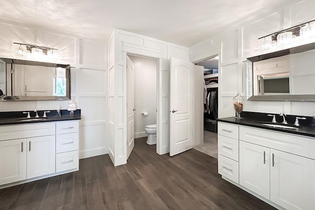 full bath with a decorative wall, wood finished floors, two vanities, toilet, and a walk in closet