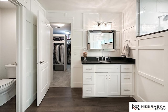 bathroom featuring vanity, toilet, a decorative wall, wood finished floors, and a walk in closet