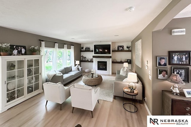 living area featuring wood finished floors, a glass covered fireplace, and baseboards