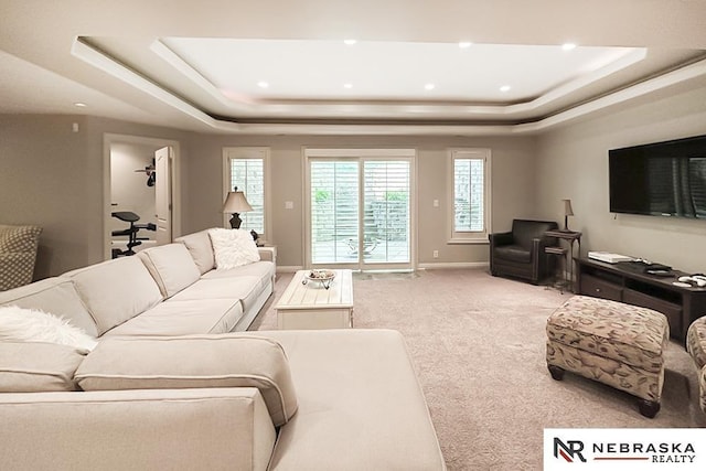 living room featuring a raised ceiling, plenty of natural light, light carpet, recessed lighting, and baseboards