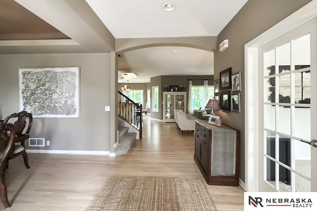 entryway with arched walkways, light wood-style flooring, baseboards, and stairway