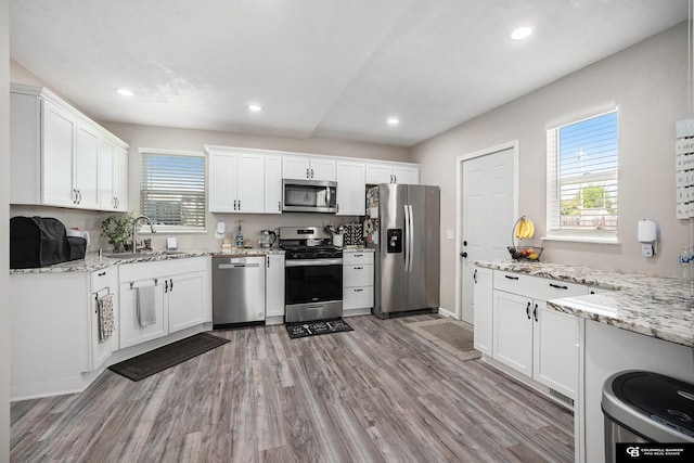 kitchen featuring stainless steel appliances, white cabinets, light wood-style flooring, a sink, and light stone counters