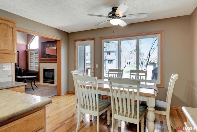 4630 Eagle Ridge Rd, Lincoln, NE 68516 - dining area with ceiling fan, light wood-type flooring, a tiled fireplace, plenty of natural light, and a textured ceiling