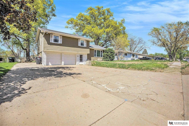 tri-level home with concrete driveway, an attached garage, brick siding, and a front yard