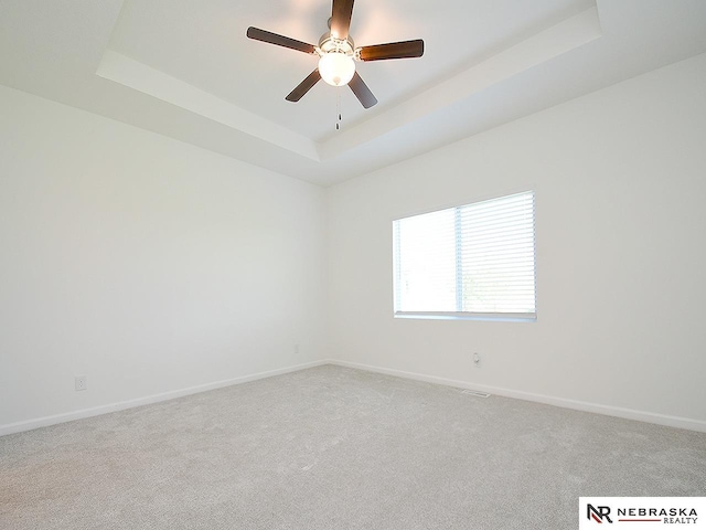unfurnished room featuring a raised ceiling, baseboards, light carpet, and a ceiling fan