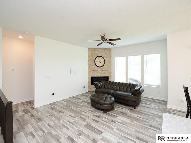 living area with a ceiling fan, light wood-type flooring, a stone fireplace, baseboards, and recessed lighting